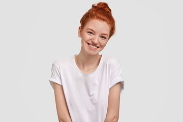 Portrait of positive glad ginger young female has warm smile, shy look, dressed casually, poses...
