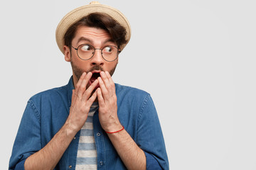 Scared surprised Caucasian male covers mouth and looks with worried expression aside, notices his...