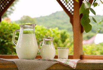 A lot of milk on the windowsill of the pergola. Two jugs of milk and a glass on the windowsill of a...