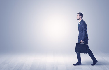 Obraz premium Successful businessman walking in front of an empty wall with briefcase on his hand 