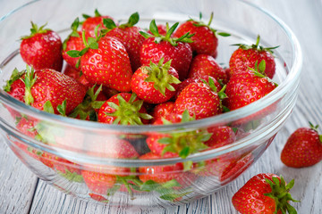Ffresh strawberries in glass saucer on wooden table.