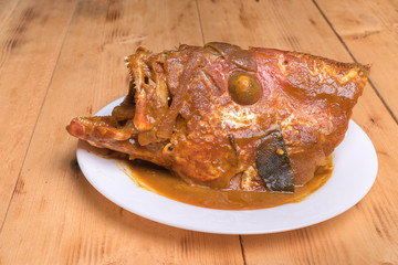 Malaysian red fish head curry in white plate over the pine wood
