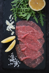 Closeup of carpaccio made of raw marbled beef and served with arugula, lemon and parmesan cheese, vertical shot, top view