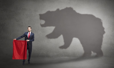 Businessman standing with red cloth in his hand and big bear shadow on his background
