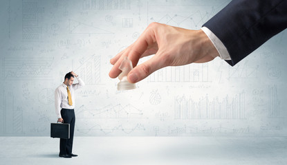 Little businessman is afraid to make the next step in his chess game with graphs, charts and...