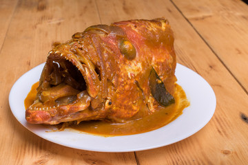 Malaysian red fish head curry in white plate over the pine wood