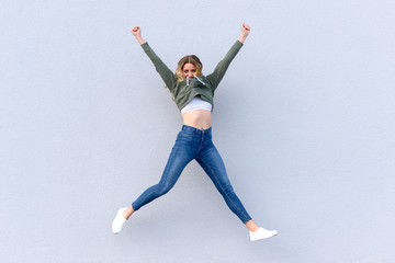 Young cheerful woman in jeans jumping into air