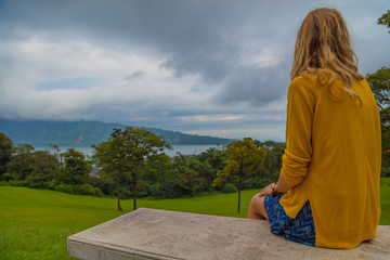 Lonesome girl sitting on a bench and looking at the nature landscape.