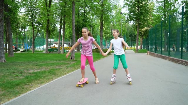 Active leisure time in park. Two caucasian, cheerful girls skating on rollers and skateboard. Wellness, health and family concept