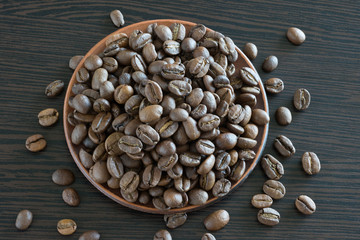 Coffee grains on a dish by close-up and on a wooden table. Kind from above.