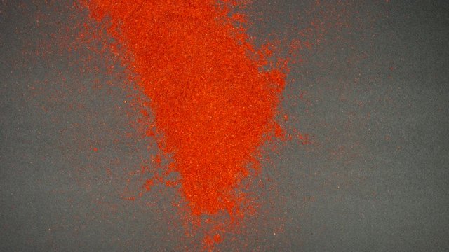 TOP VIEW: Flow of red pepper falls on a black table - Slow Motion