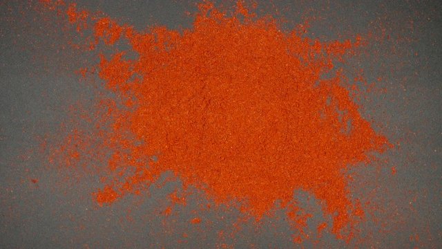 TOP VIEW: Red pepper powder falling and splashing on a black table - Slow Motion