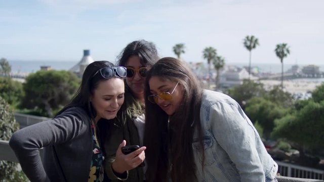 Group Of Girlfriends Look At Their Vacation Photos On Smartphone Together, Santa Monica Pier In Background - Shot On Red Scarlet-W Dragon In 4K, Slow Motion