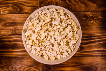 Ceramic plate with popcorn on wooden table. Top view