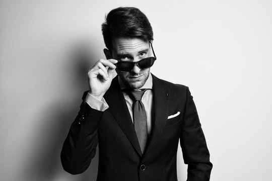 Black and white portrait of a stylish handsome young man wear suit and sunglasses in studio
