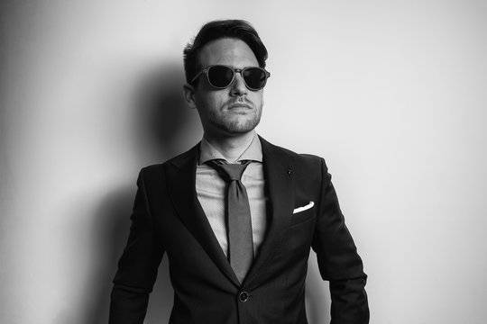 Black and white portrait of a stylish handsome young man wear suit and sunglasses in studio