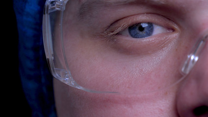 Surgeon or doctor wearing goggles, blue eyes, in medical cap, dark background, macro.
