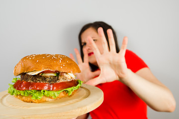 Young fat girl closes his hands for fear of a hamburger on gray background