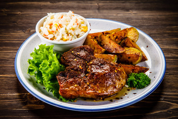 Grilled steak with baked potatoes and vegetables served on wooden table