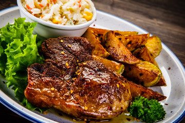 Grilled steak with baked potatoes and vegetables served on wooden table