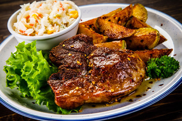 Grilled steak with baked potatoes and vegetables served on wooden table