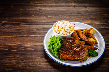 Grilled steak with baked potatoes and vegetables served on wooden table