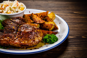 Grilled steak with baked potatoes and vegetables served on wooden table