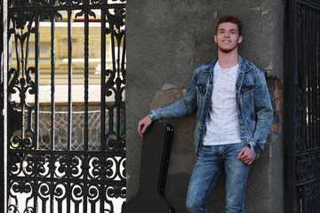 Young cheerful guy with red hair at the gate with a guitar in the case