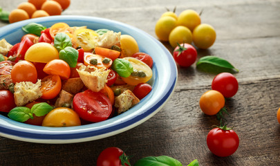 Fototapeta na wymiar Panzanella Tomato salad with red, yellow, orange cherry tomatoes, capers, basil and ciabatta croutons. summer healthy food.