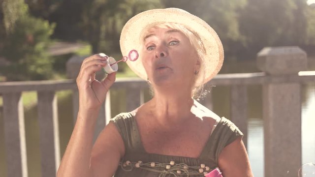 Happy senior woman with bubble blower. Cheerful elderly woman having fun blowing soap bubbles outdoors.