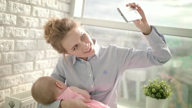 Happy woman taking selfie photo with sleeping baby. Smiling mother take selfie on phone. Business mother taking mobile photo with daughter. Happy motherhood. Family portrait