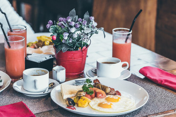 Breakfast with fried eggs, juice, coffee and fruits on wooden table in the tropical restaurant, Bali island.