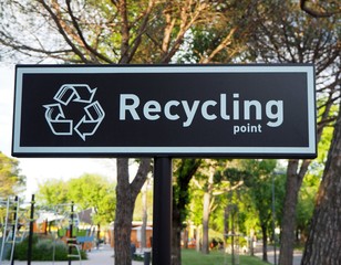Recycling point sign ,words and symbol in white color on black background. Blurred public park on behind 
