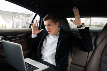 Go on and do not give up! Attractive young intelligent man going to the work in the office by car and having troubles, while using his computer.