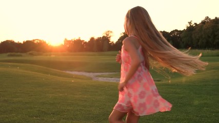 Girl in dress is spinning outdoors. Little girl is dancing on grass. Child is outdoors, summer.