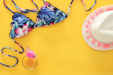 Top view of fashion female swimsuit bikini and white fedora hat on yellow wooden background. Summer beach vacation concept.