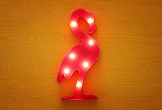 a plastic flamingo lamp with leds over yellow wooden background. holiday summer concept.