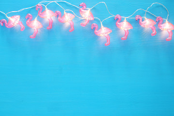 a plastic flamingo garland lights over blue wooden background. holiday summer concept. © tomertu