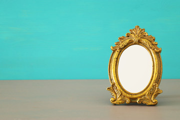 Vintage blank gold photo frame over wooden table. Ready for photography montage.