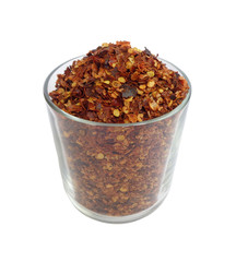Transparent glass cup filled with dried and cruched red hot pepper isolated on white background
