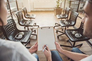 Woman and male writing on paper while sitting in empty room with headsets on chairs