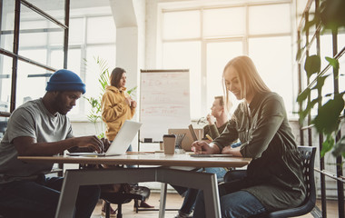 Outgoing lady telling with calm man while writing information at table. He using notebook computer. Positive colleagues communicating near board