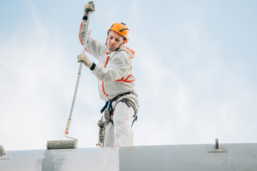 Industrial climber in helmet and uniform painting water tower. Professional Painter working on...