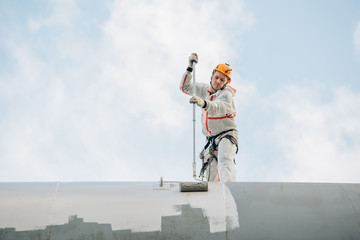 Industrial climber in helmet and uniform painting water tower. Professional Painter working on...