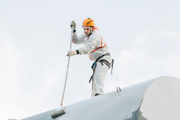 Industrial climber in helmet and uniform painting water tower. Professional Painter working on...