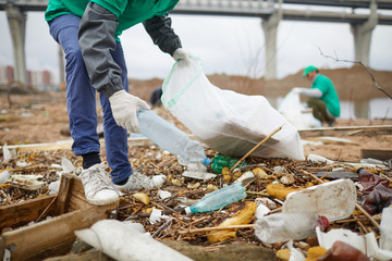 Worker of nature protection company taking plastic bottle from littered ground