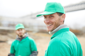 Happy young man in green uniform and his colleague during nature protection work outdoors