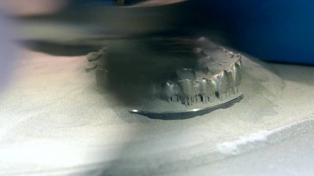 Man is cleaning wit brush object printed on 3d metal printer from metal powder close-up. Dental crowns created in laser sintering machine. DMLS, SLM, SLS additive technology. 4.0 industrial revolution