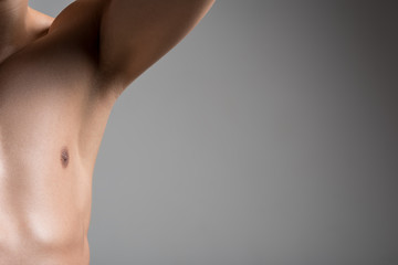 Close up half of torso of young man with smooth armpit. He is standing with raised arm against light wall and demonstrating his hairless underarm. Laser hair removal concept. Copy space in right side