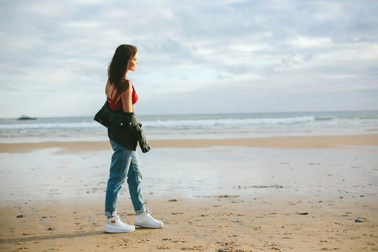 Young woman wearing leather jacket walking on ocean beach.